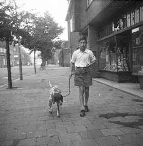 831224 Afbeelding van Peter van der Linden, wandelend met leenhond Job, in het Ondiep te Utrecht; rechts de winkel van ...